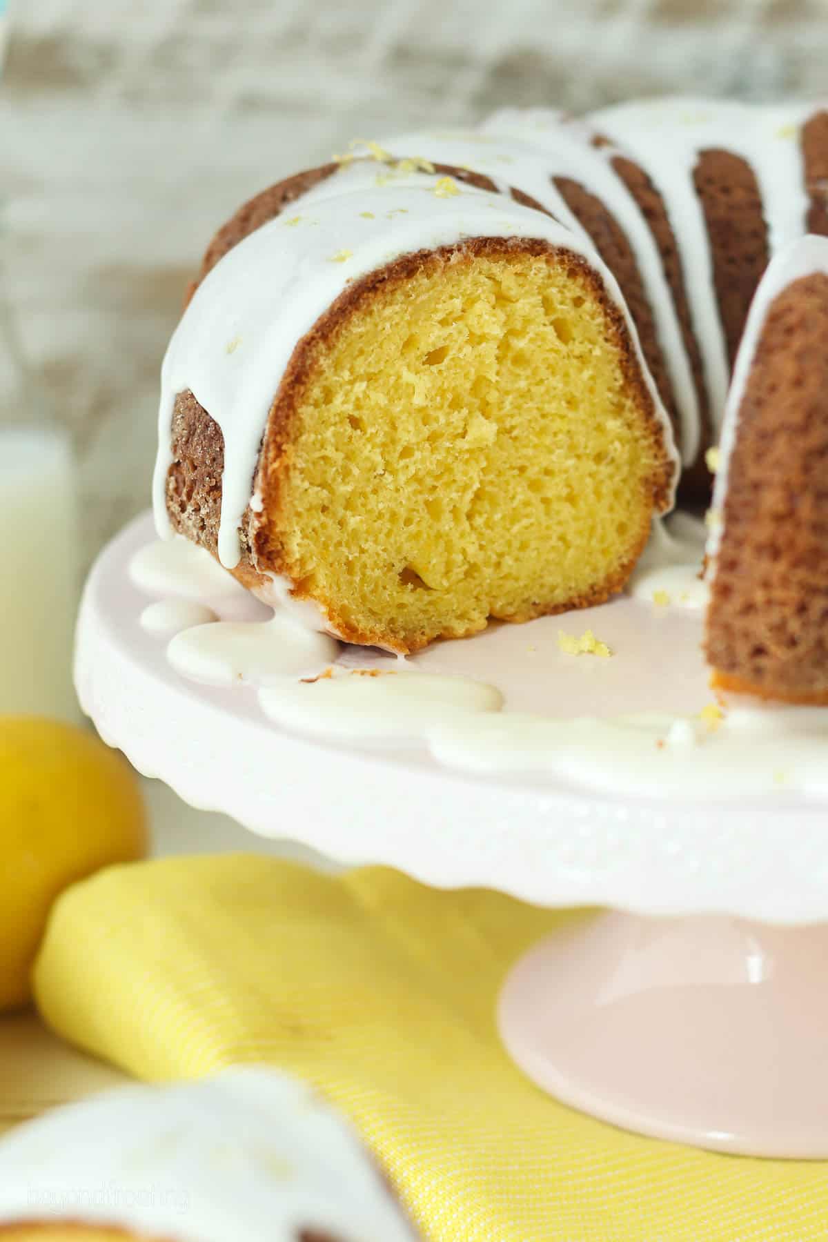 side view of a lemon bundt cake with a slice out on a cake stand