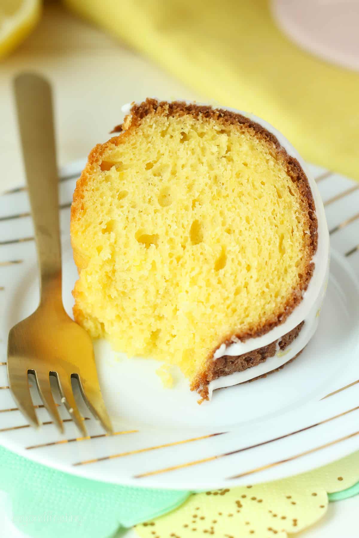 overhead shot of a slice of lemon bundt cake on a white and gold plate with a gold fork.