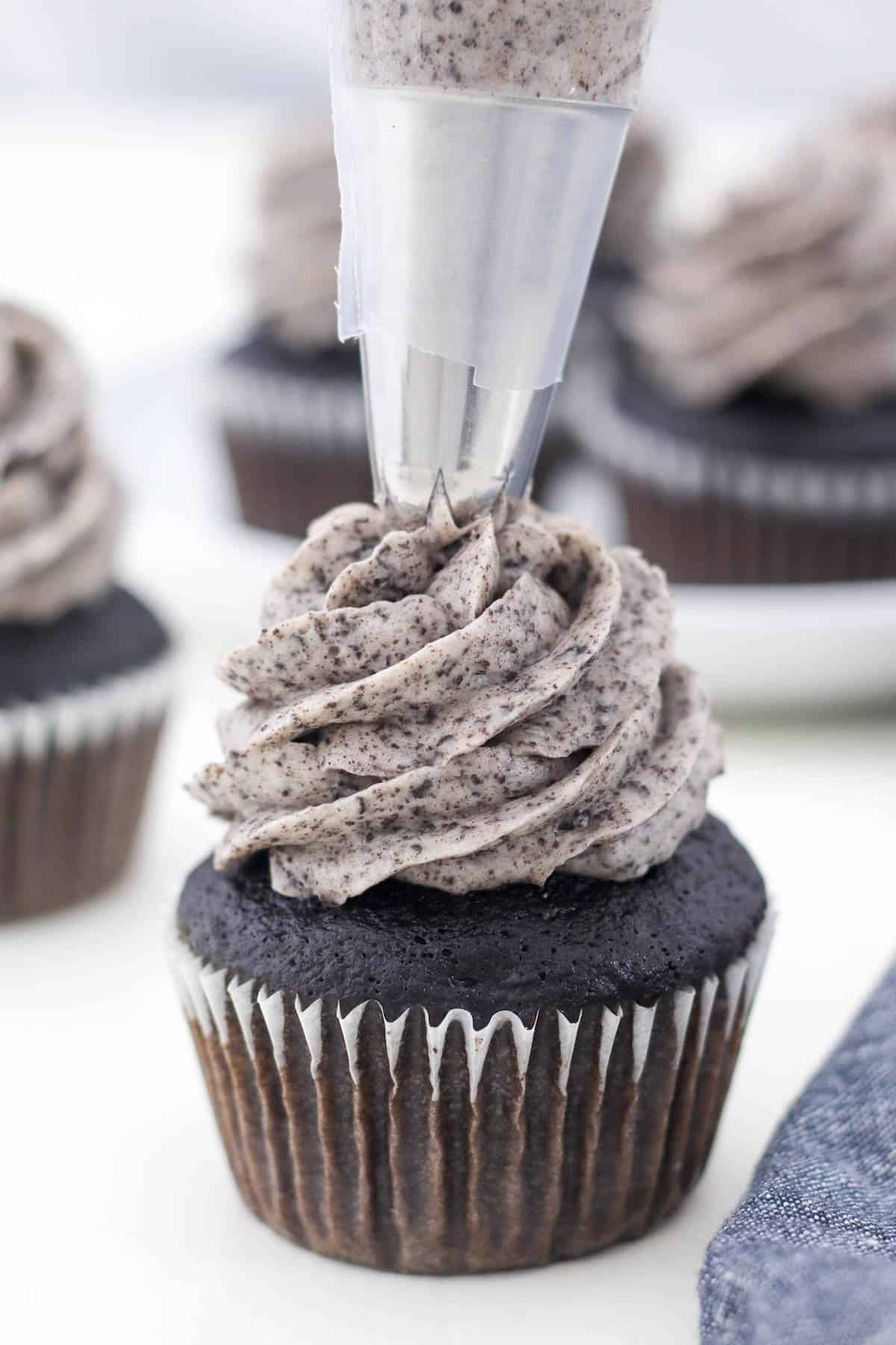Oreo frosting being piped onto a chocolate cupcake