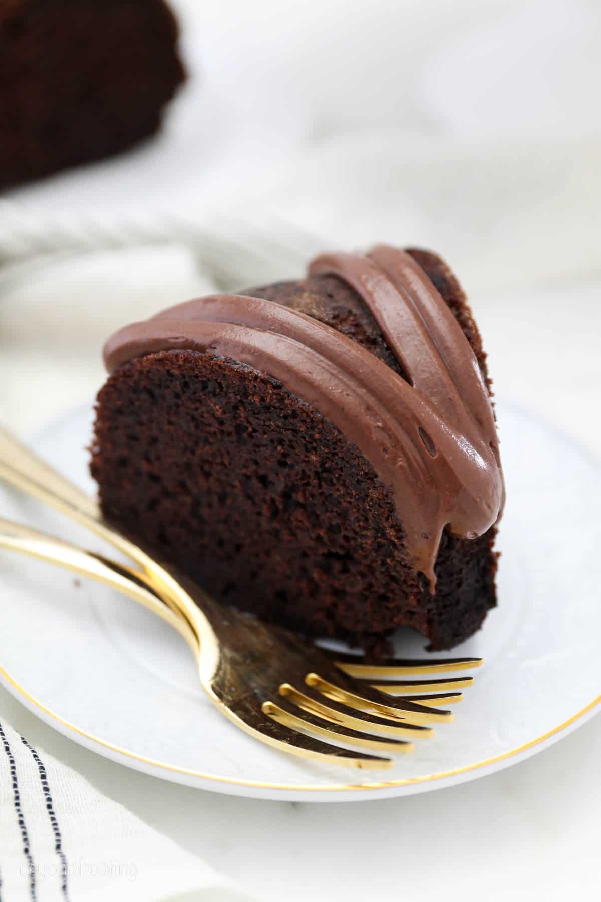 overhead of a slice of chocolate cake topped with chocolate cream cheese frosting on a plate with two gold forks..