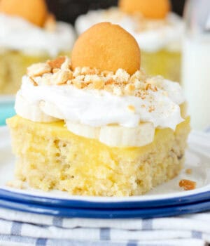 closeup of a slice of banana pudding poke cake topped with a Nilla wafer and whipped cream.