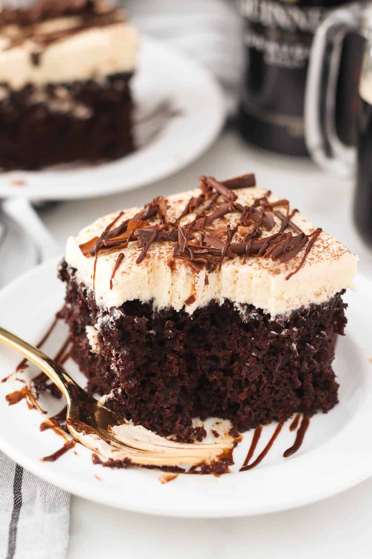 a square of chocolate cake topped with baileys Irish cream frosting on a white plate with a fork.