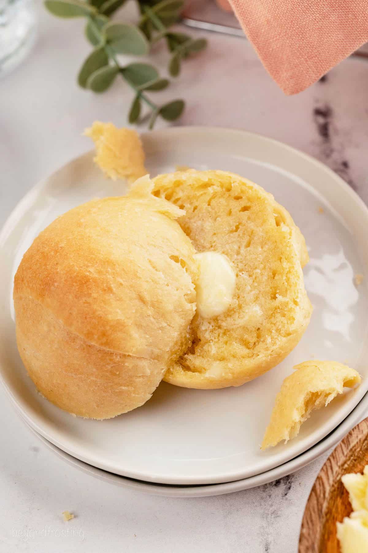 Two halves of a dinner roll on a white plate, with a pat of butter melting on one half.