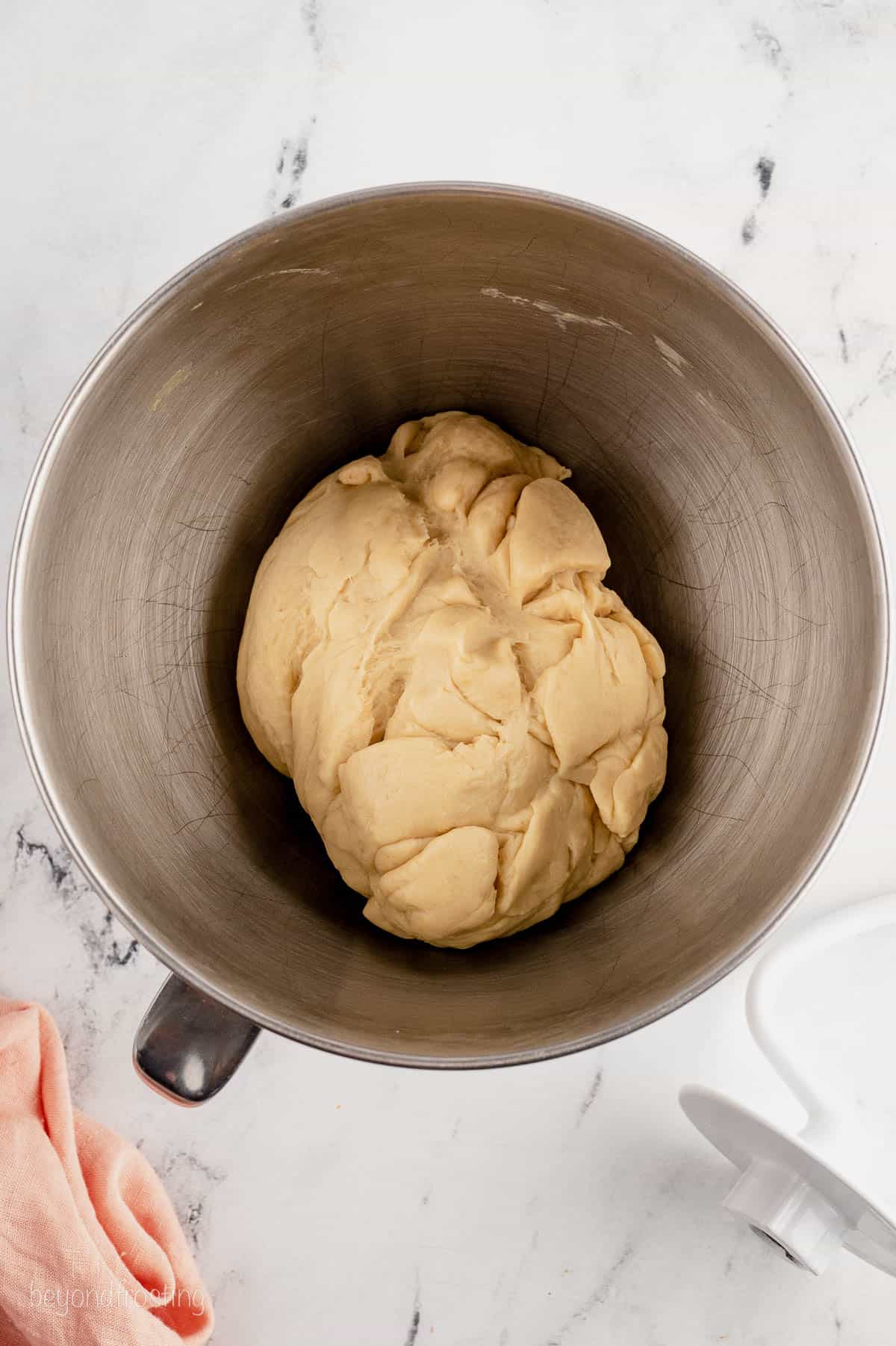 The dough for dinner rolls in a ball inside a mixing bowl.