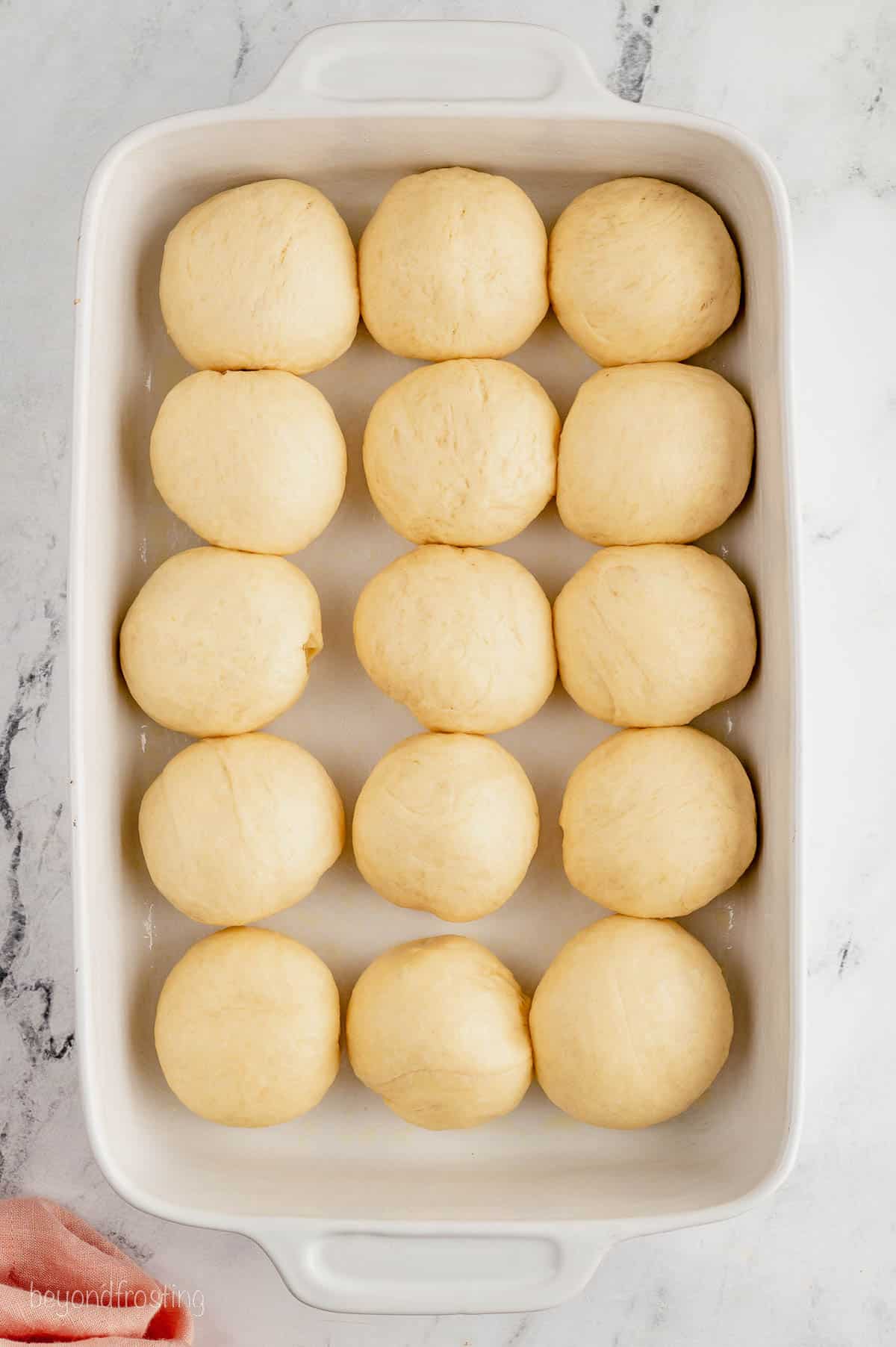 Dinner roll dough balls after the rise, arranged in a ceramic baking dish.