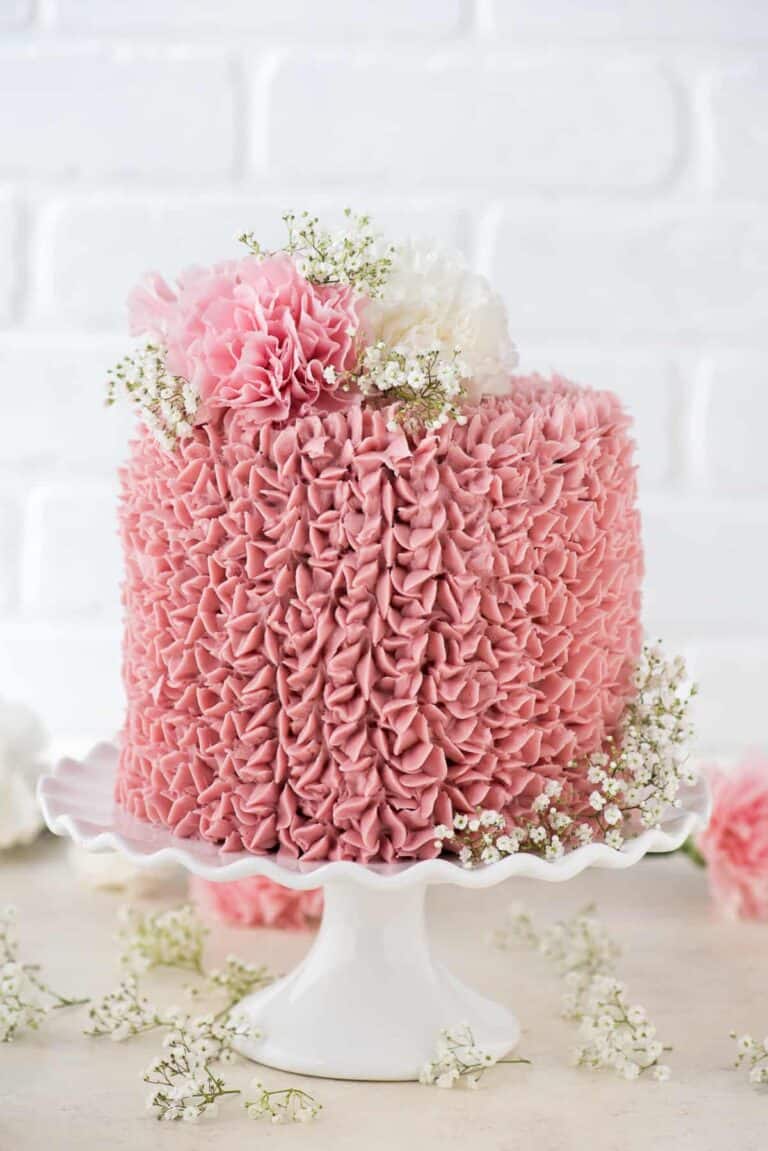 A frosted raspberry cake decorated with fresh flowers