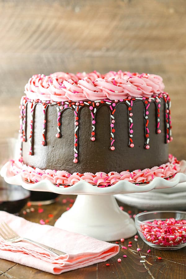 Chocolate Cake decorated with pink frosting, chocolate drip and sprinkles on a white cake stand