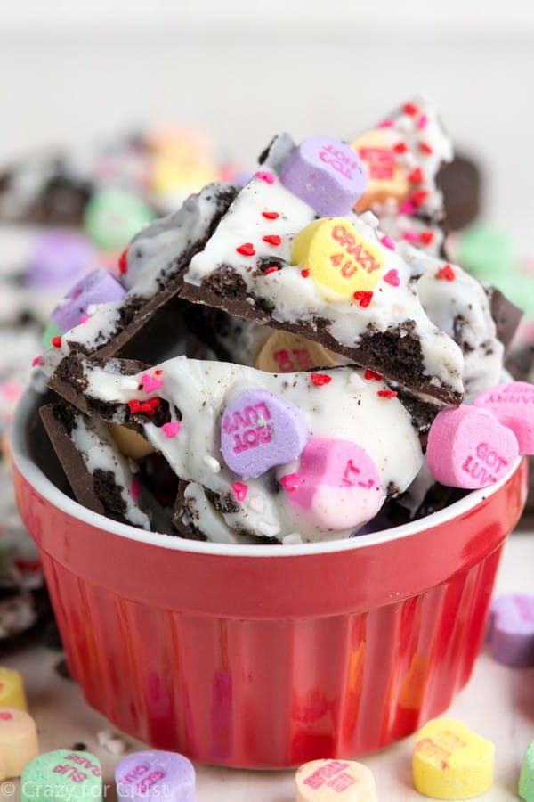 Oreo bark decorated for valentine's day with sprinkles and conversation hearts in a red cup