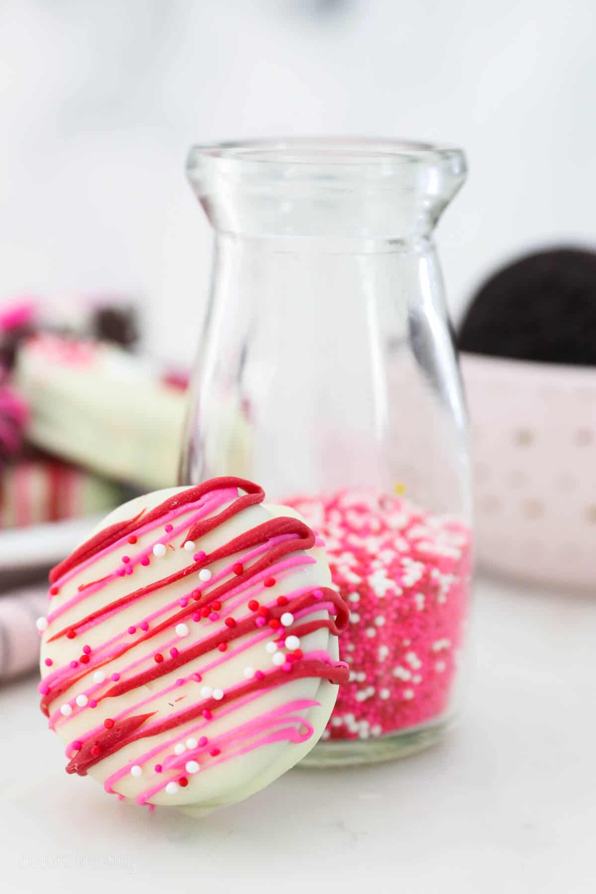 A chocolate dipped Oreos decorated for Valentine's day, covered in red and pink drizzle with sprinkles/