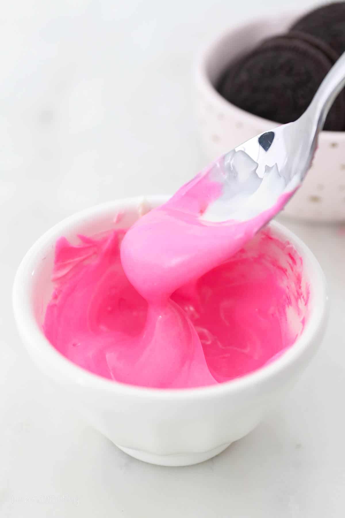 a bowl of pink colored white chocolate dripping off a spoon