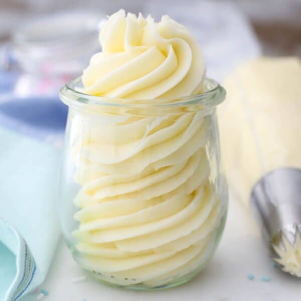 A small jar of piped vanilla frosting with a teal napkin and piping bag next to it