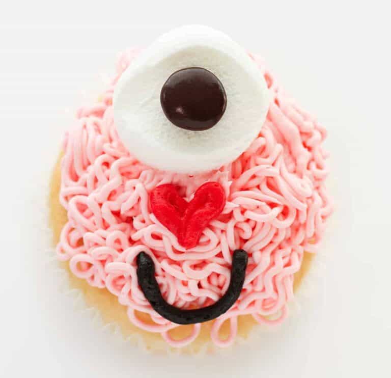 A cupcake decorated with a marshmallow, heart and smiley face