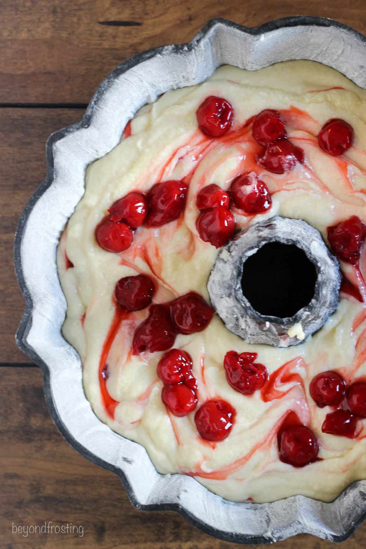 overhead of a bundt pan with cake batter swirled with cherries and cherry juice.