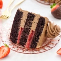 A slice of frosted chocolate strawberry layer cake with strawberry filling, laying on its side on a plate.