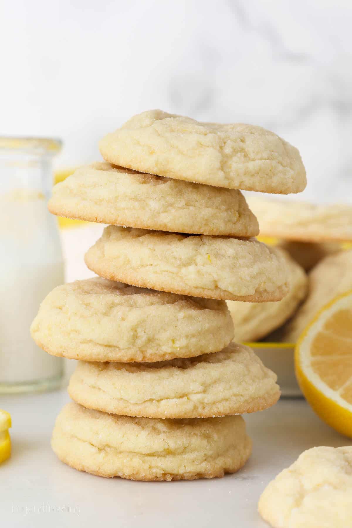 A tall stack of lemon cookies with a milk jug and lemons in the background.