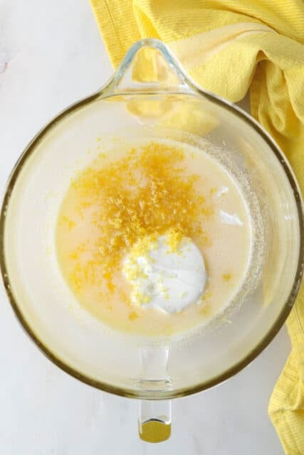 Lemon zest added to a mixing bowl with wet cake batter ingredients.