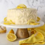 Frosted lemon curd layer cake on a cake stand garnished with lemon slices.