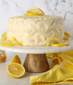 Frosted lemon curd layer cake on a cake stand garnished with lemon slices.