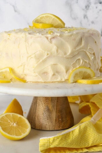 Frosted lemon curd layer cake on a cake stand garnished with lemon slices.