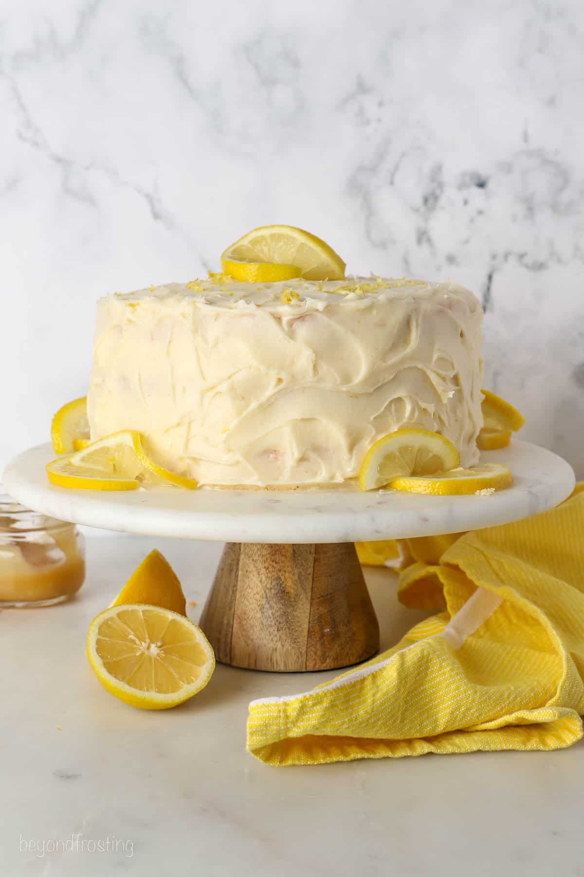 Frosted lemon curd layer cake on a cake stand garnished with lemon slices.