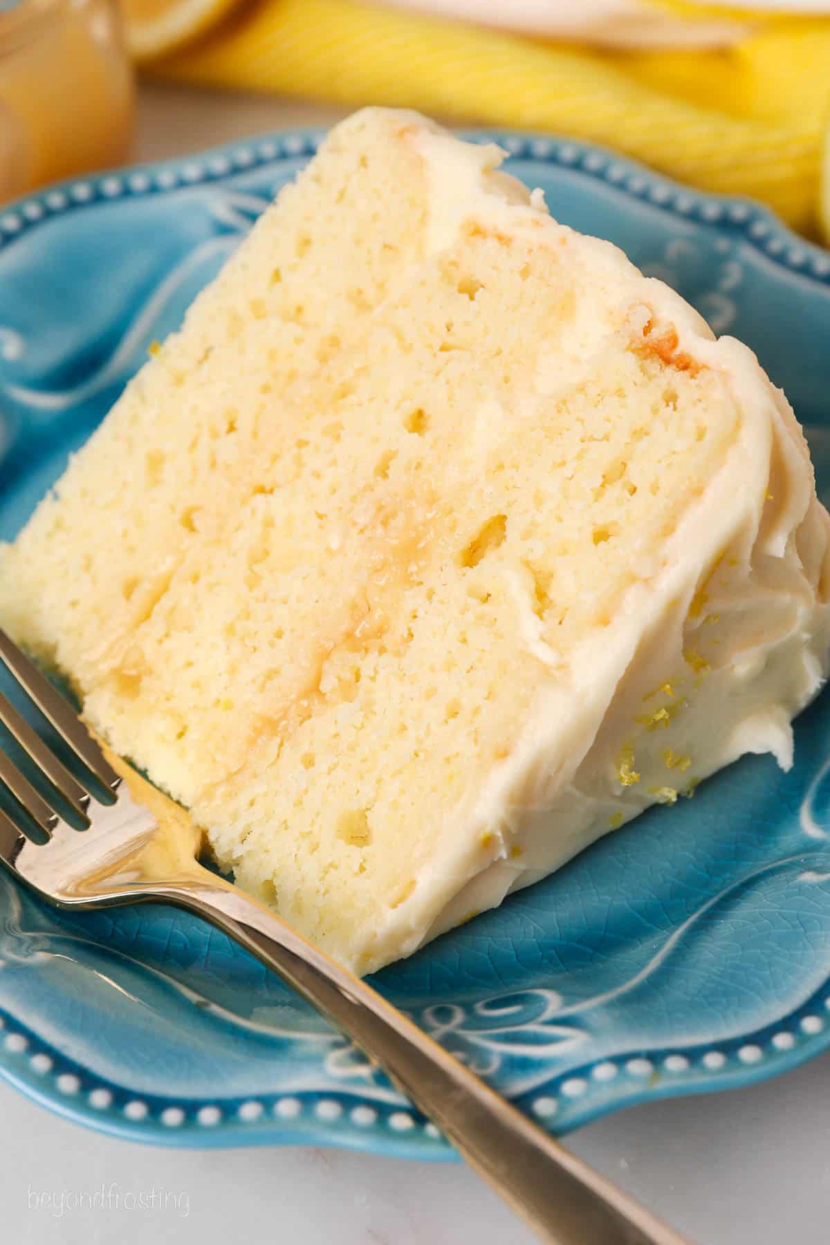 A slice of lemon layer cake on a blue plate next to a fork.