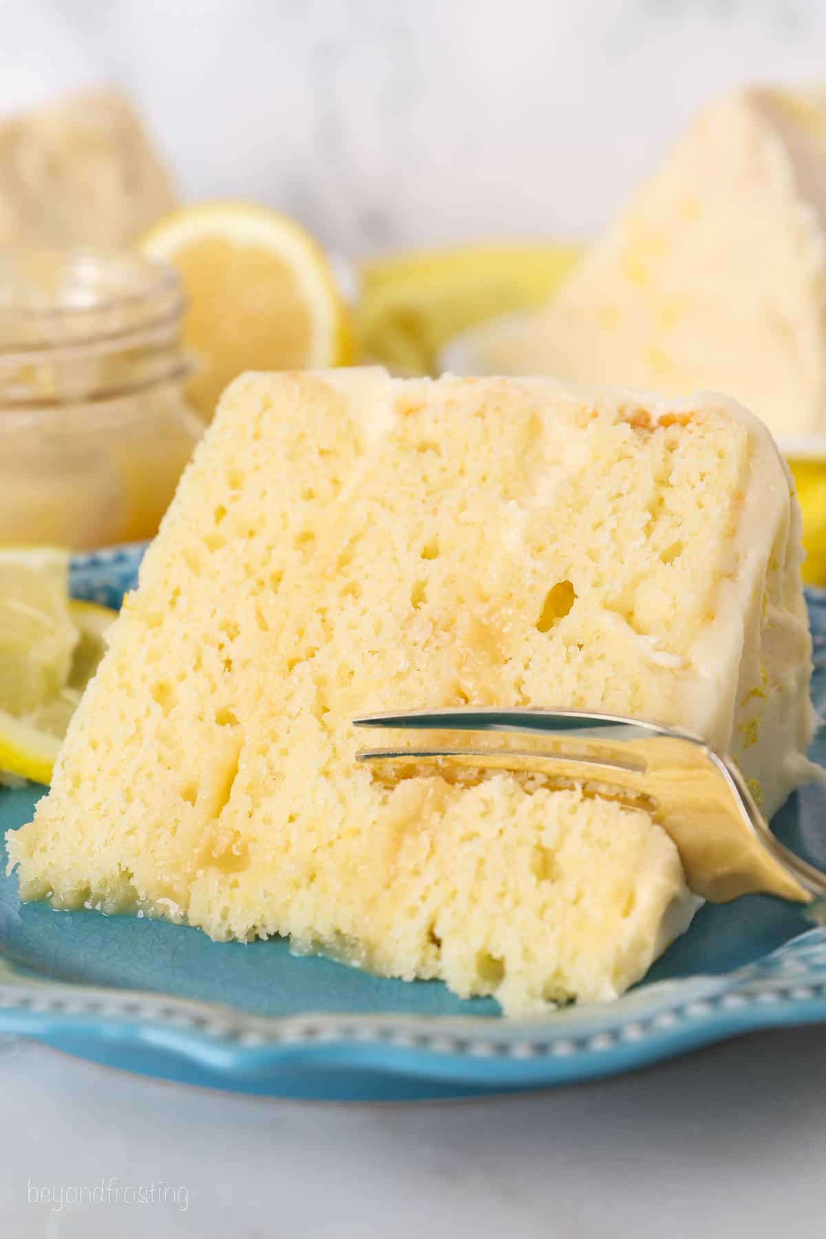 A fork cuts into the corner of a slice of lemon layer cake on a blue plate.