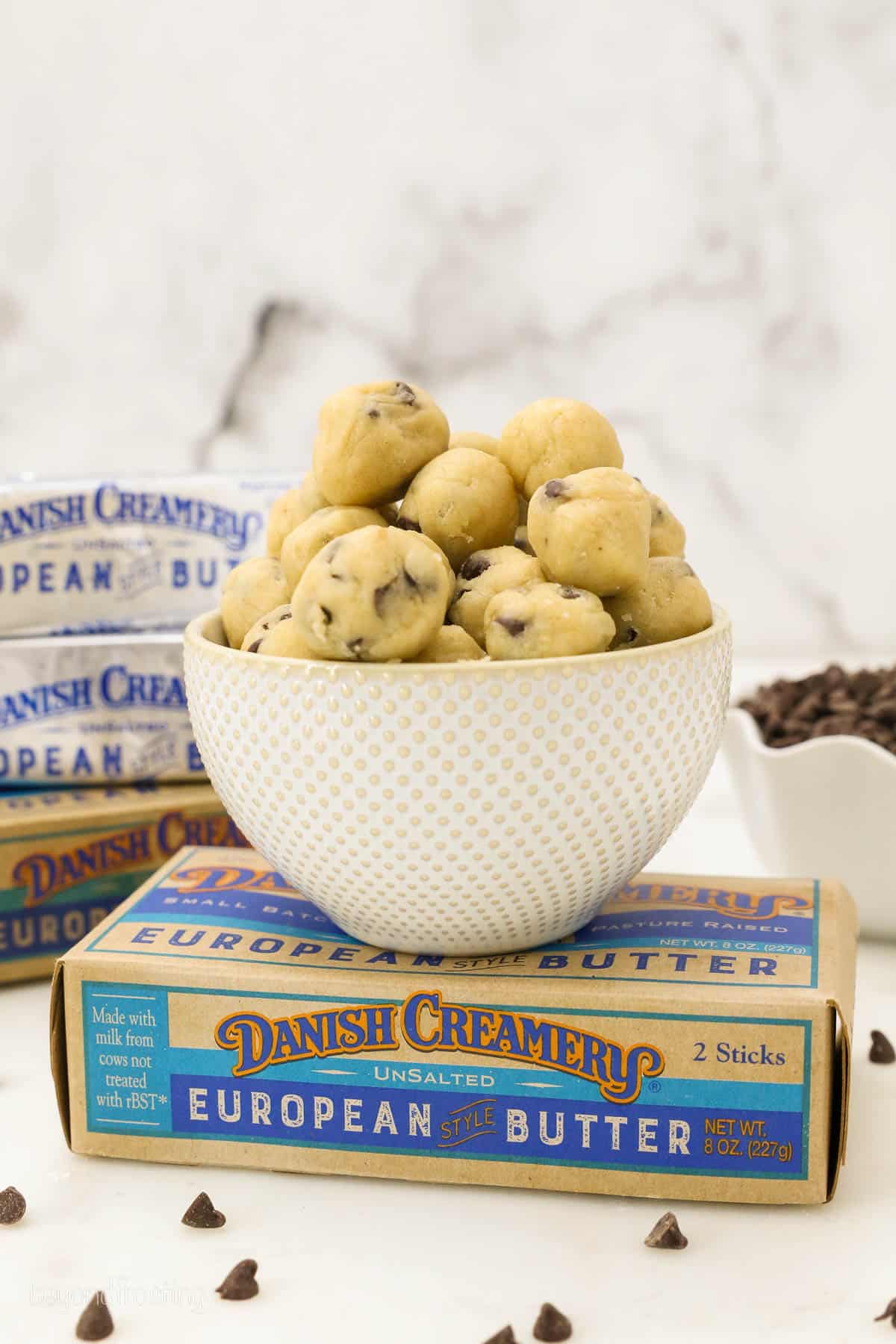 a bowl of cookie dough balls set on a box of butter.