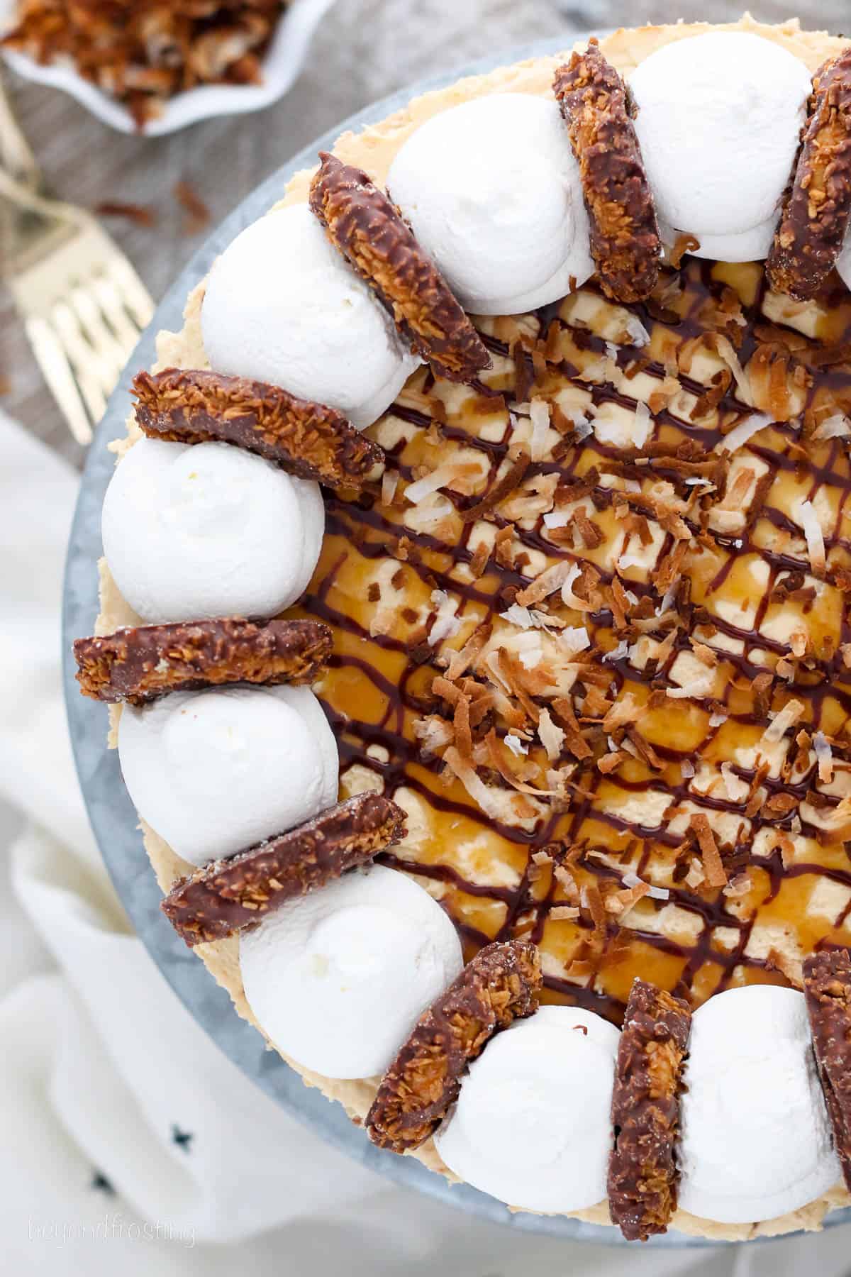 overhead of a whole Samoa cheesecake topped with caramel and chocolate, coconut, and whip.