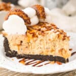 closeup side view of a slice of caramel cheesecake with an Oreo crust topped with whipped cream and cookies.