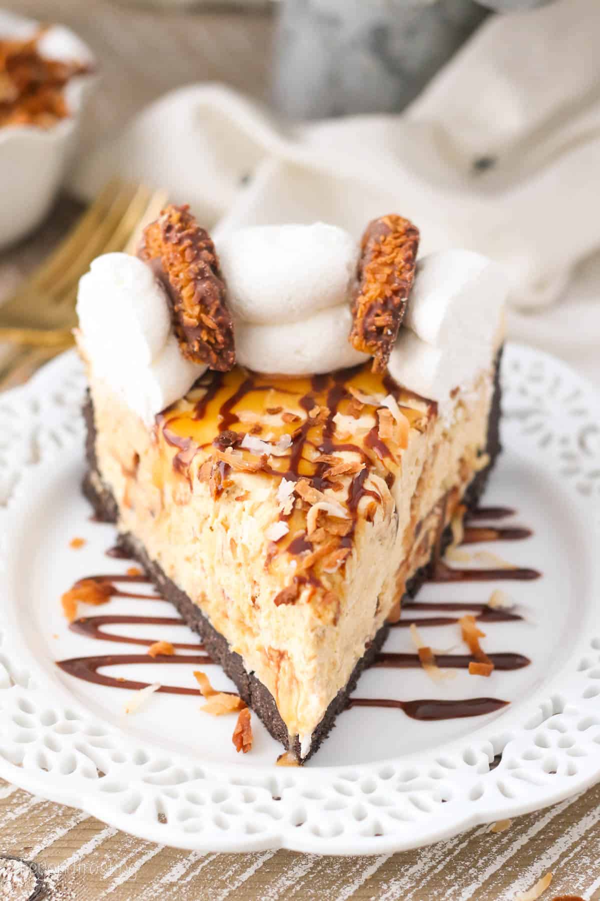 front view of a slice of caramel cheesecake with whipped craem and Samoa cookies.