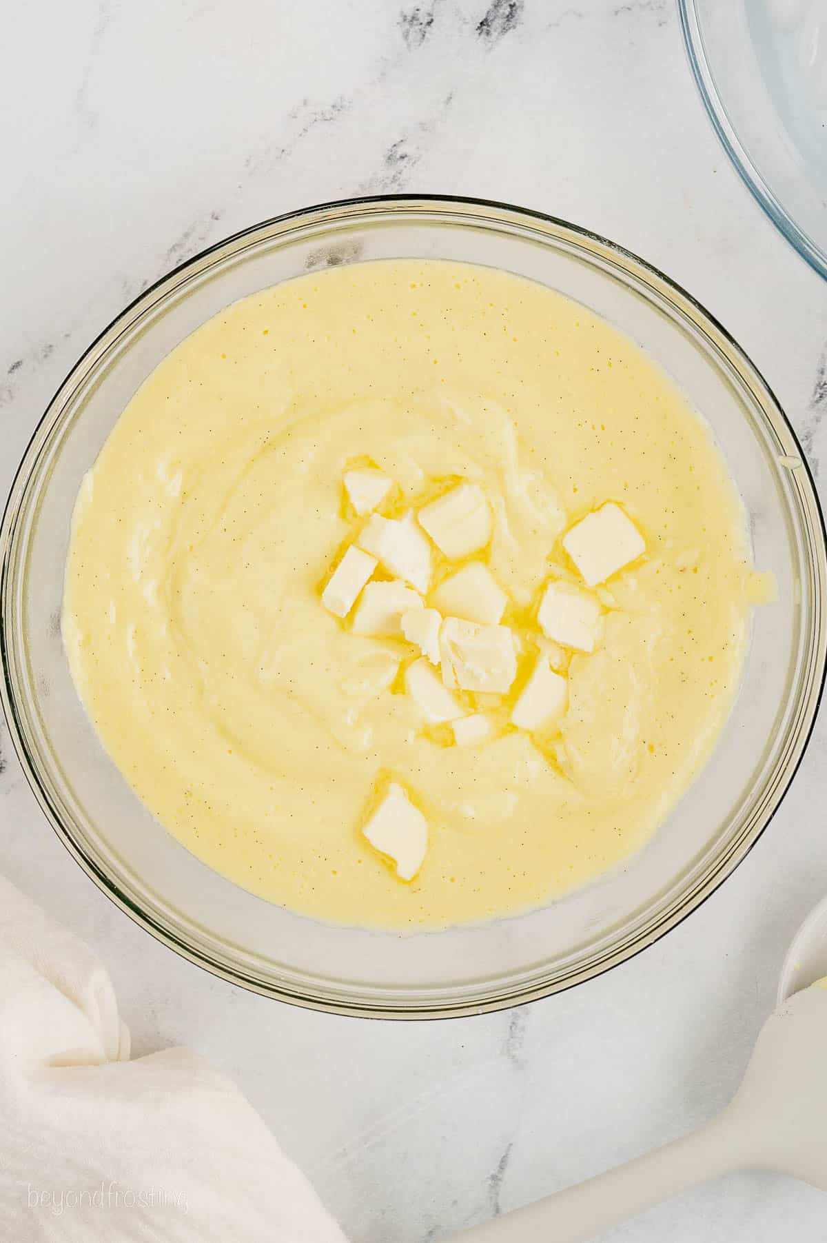 Cubed butter added into a bowl of warm pastry cream.