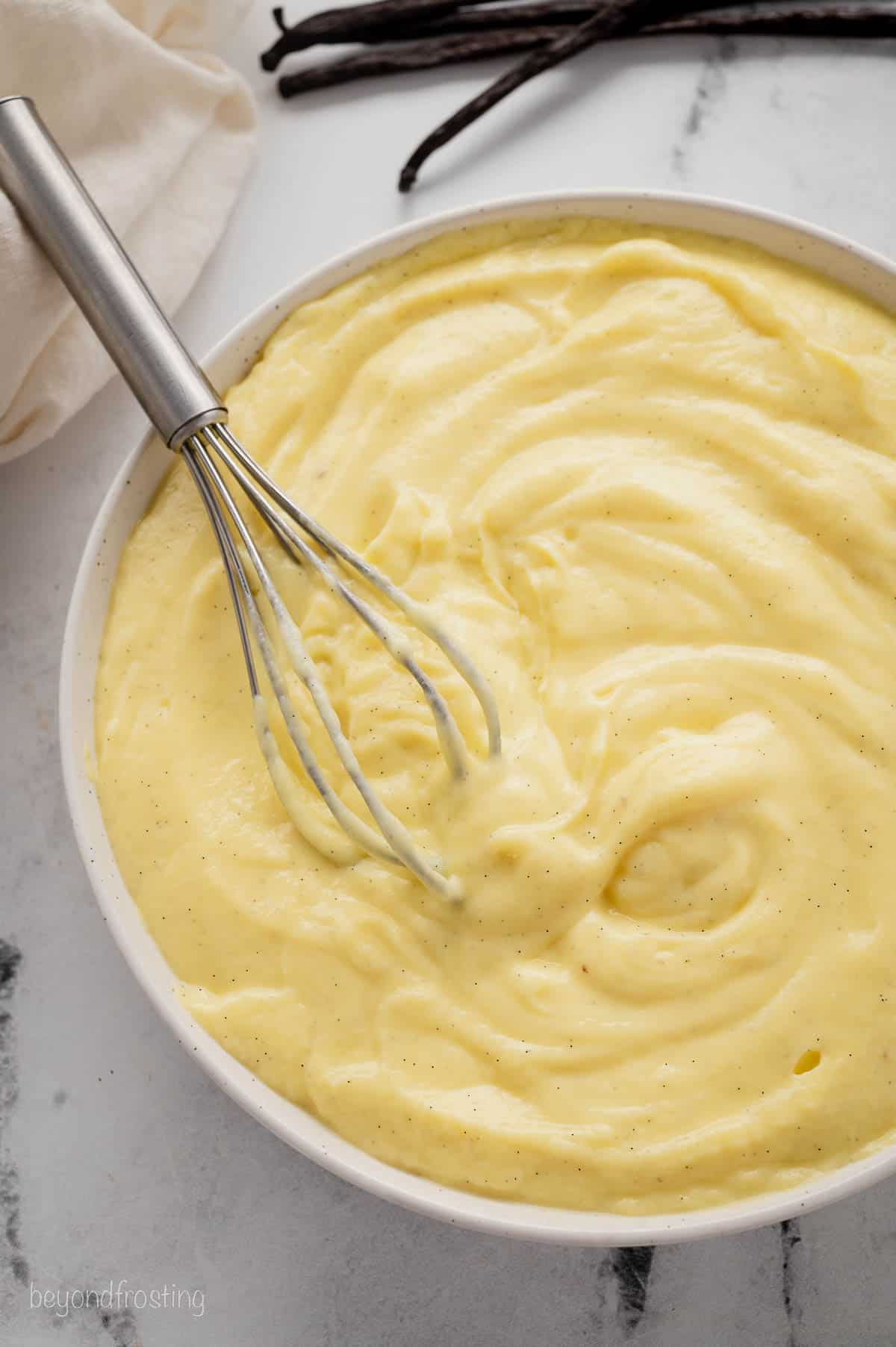 Overhead view of a whisk resting in a large bowl of pastry cream.