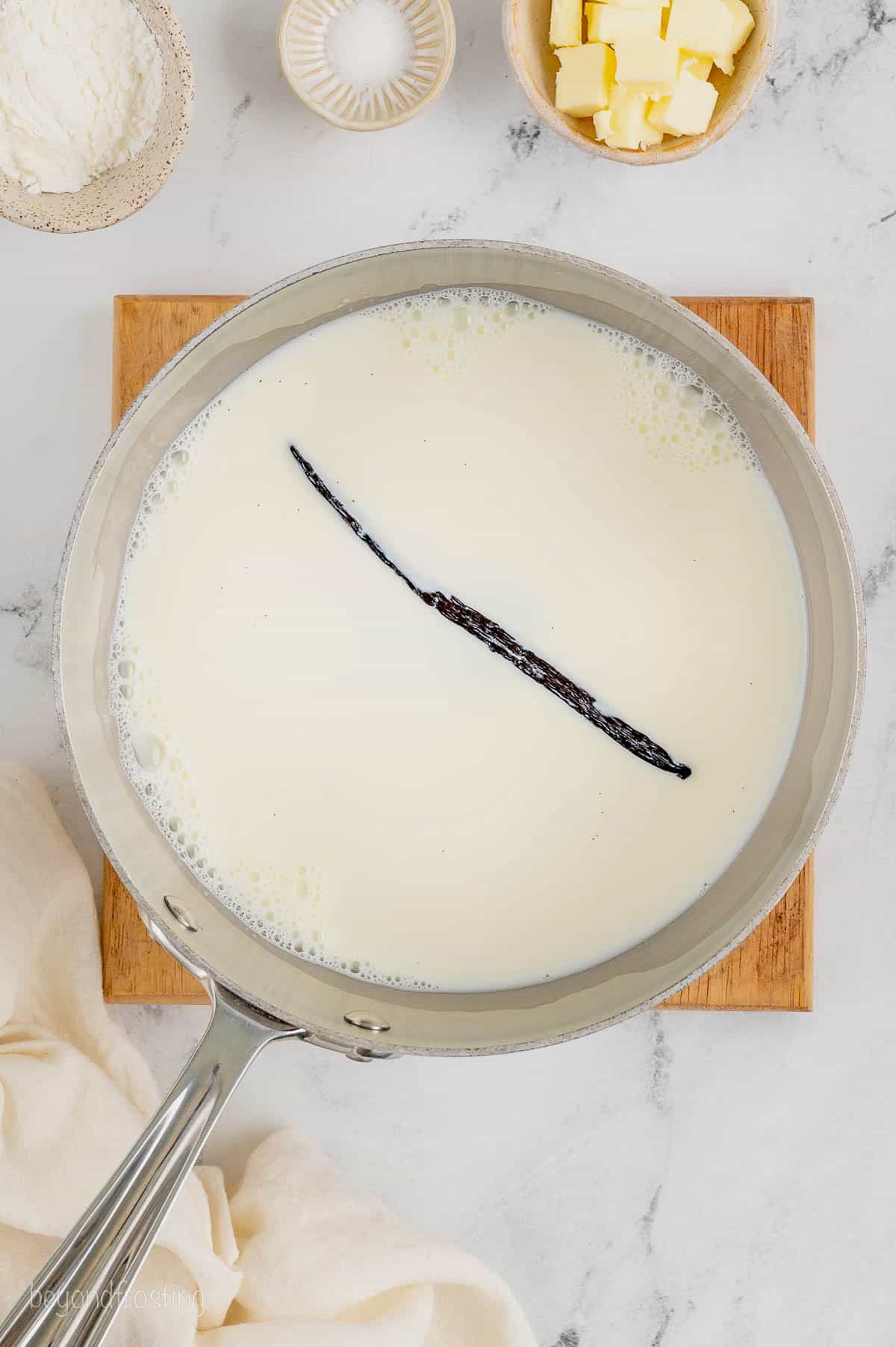Milk and vanilla bean simmering in a saucepan.