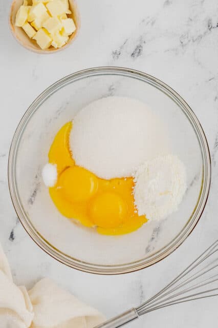 Egg yolks combined with other custard ingredients inside a mixing bowl.