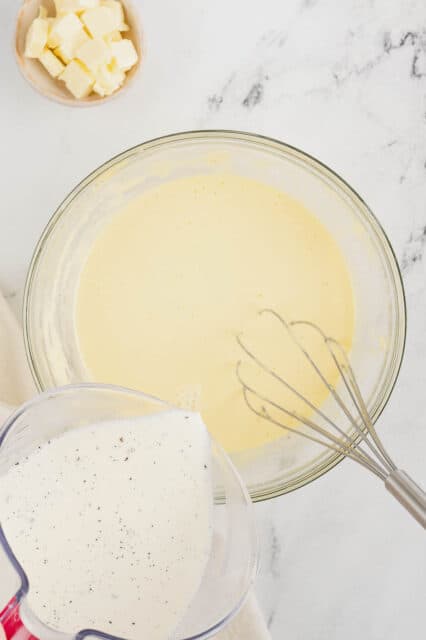 Warm vanilla-infused milk is poured into a bowl of custard mixture, to temper the eggs.