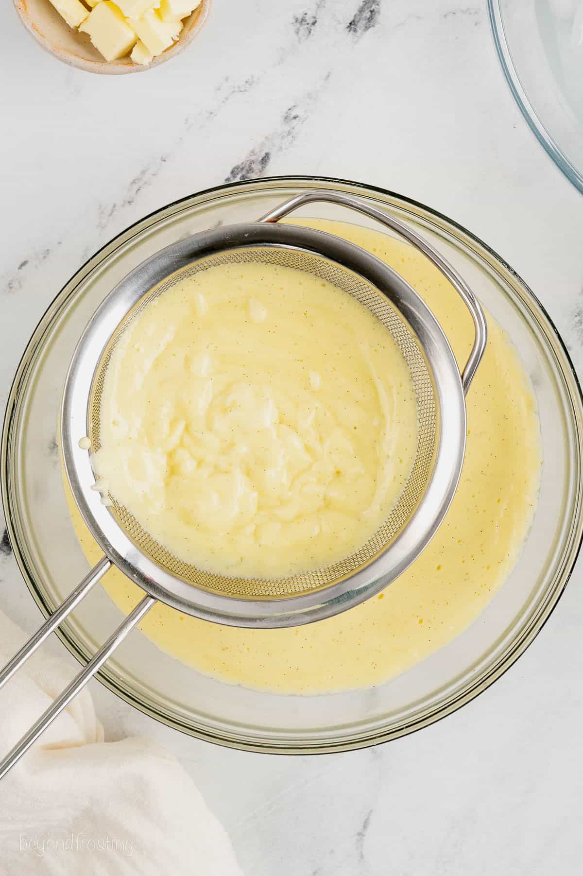 Pastry cream is strained through a mesh sieve and into a large glass bowl.