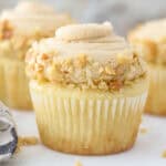 closeup side view of a vanilla cupcake topped with frosting and crushed peanuts.