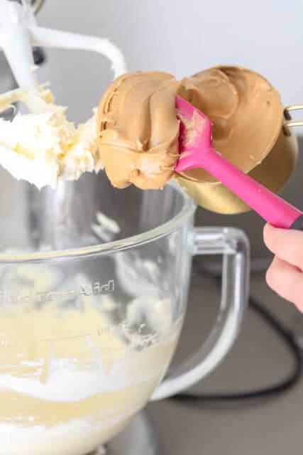 peanut butter being added to a bowl of frosting.