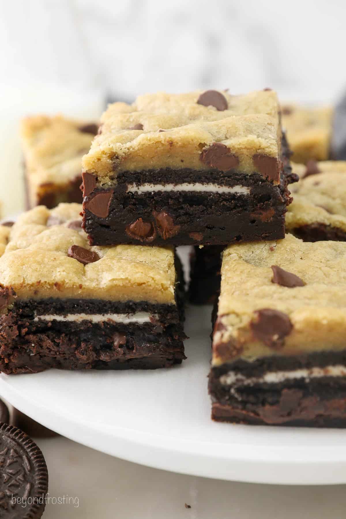 Three slutty brownies stacked on a white plate with more brownies in the background.
