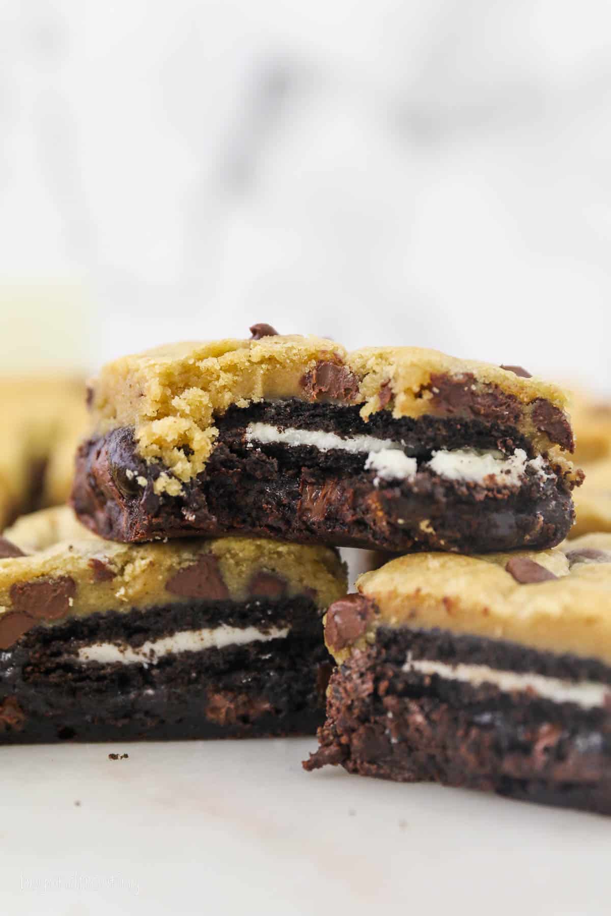 Three slutty brownies stacked on a white countertop, with a bite missing from the top brownie.