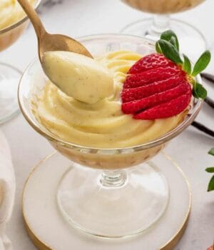 A spoon dipped into pastry cream in a coup glass, garnished with a sliced strawberry.