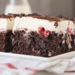 closeup side view of a slice of chocolate poke cake with cherry pie filling on a plate.