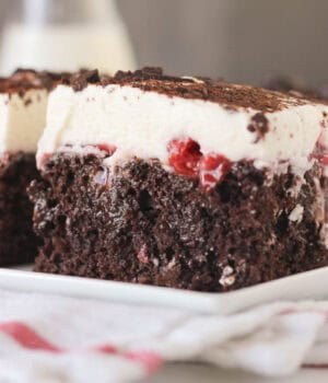 closeup side view of a slice of chocolate poke cake with cherry pie filling on a plate.