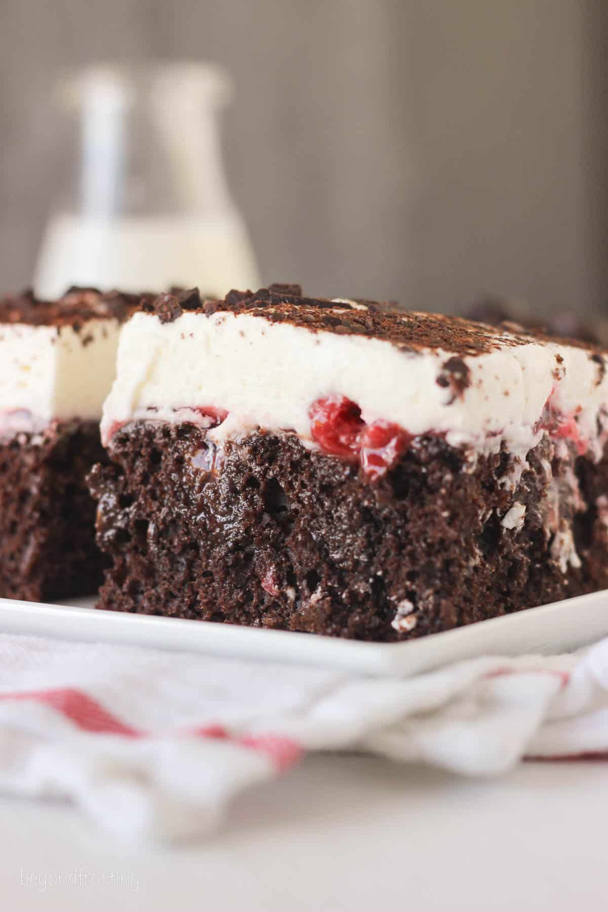 side view of a square slice of black forest poke cake on a white plate.