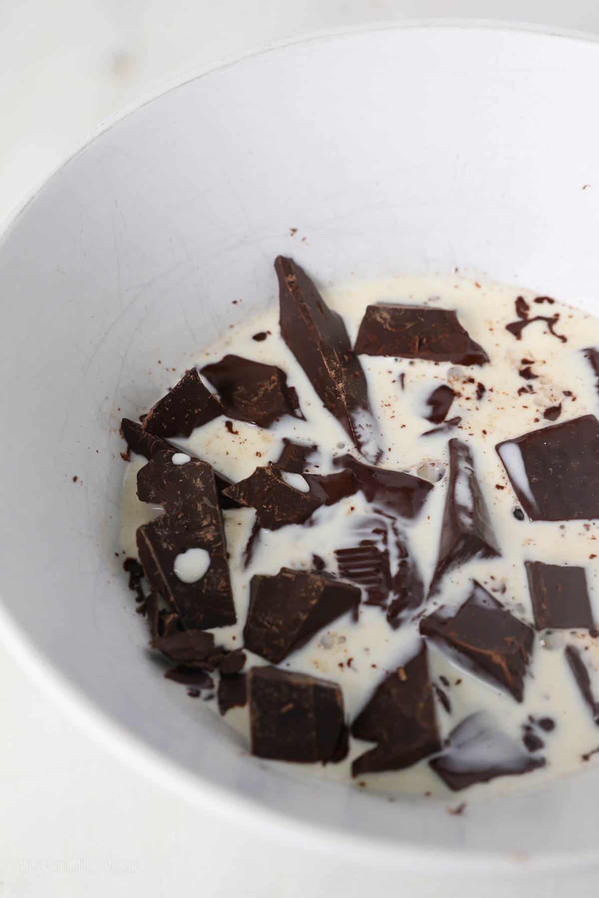 This chocolate mousse cake recipe is easy to make, with layers of moist chocolate cake, fluffy chocolate mousse, and creamy chocolate ganache. Chopped chocolate and heavy cream combined in a white bowl.