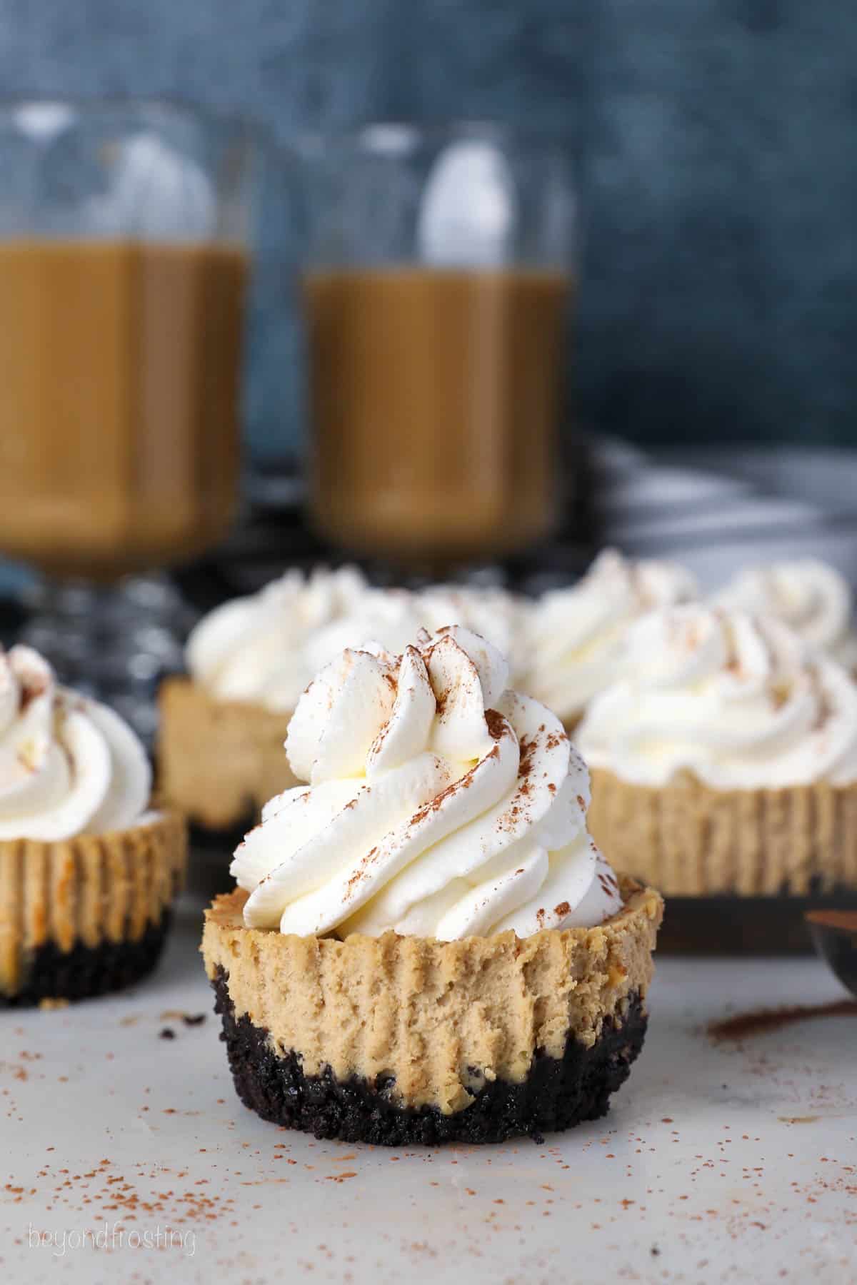 Mini coffee cheesecakes dusted with cocoa powder and coffees in the background