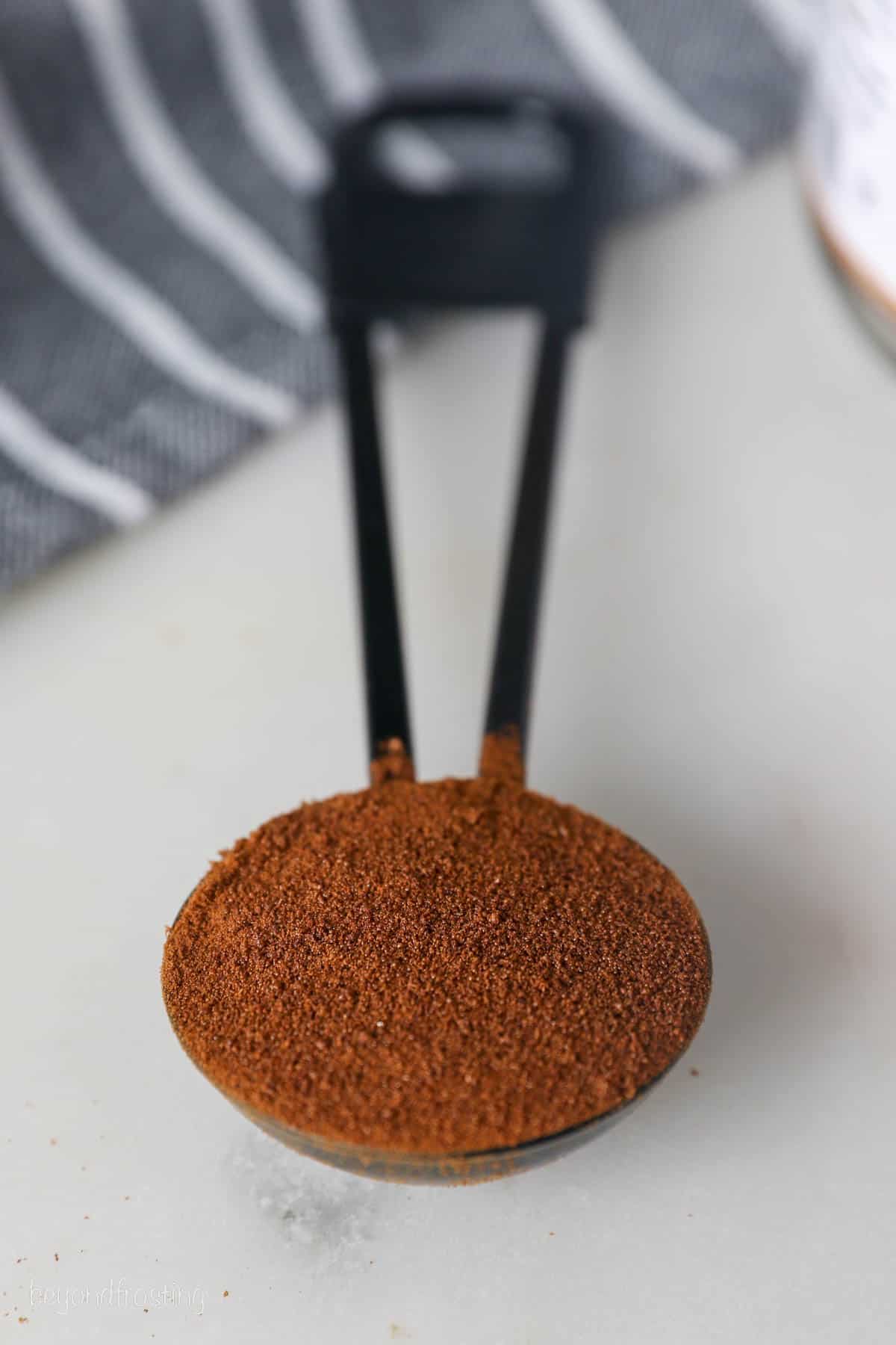 a black teaspoon measuring spoon filled with espresso powder