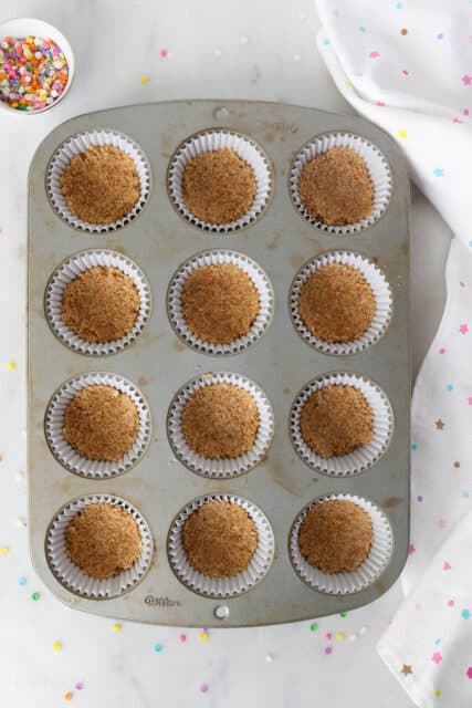 Nilla wafer crust pressed into the bottoms of cupcake liners in a 12-well cupcake pan.