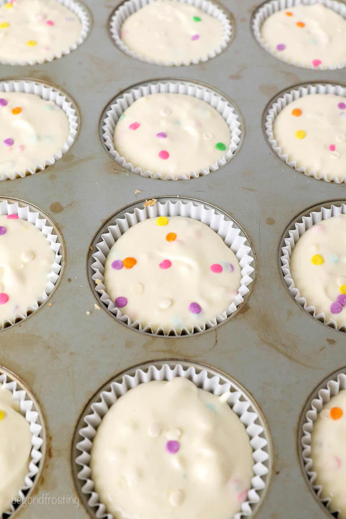 Close up of a lined cupcake pan filled with funfetti cheesecake batter.