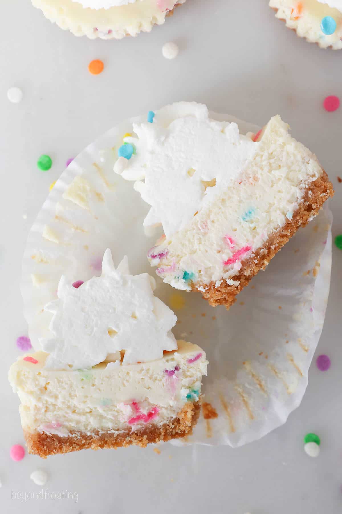 Overhead view of an unwrapped, frosted mini funfetti cheesecake cut in half.